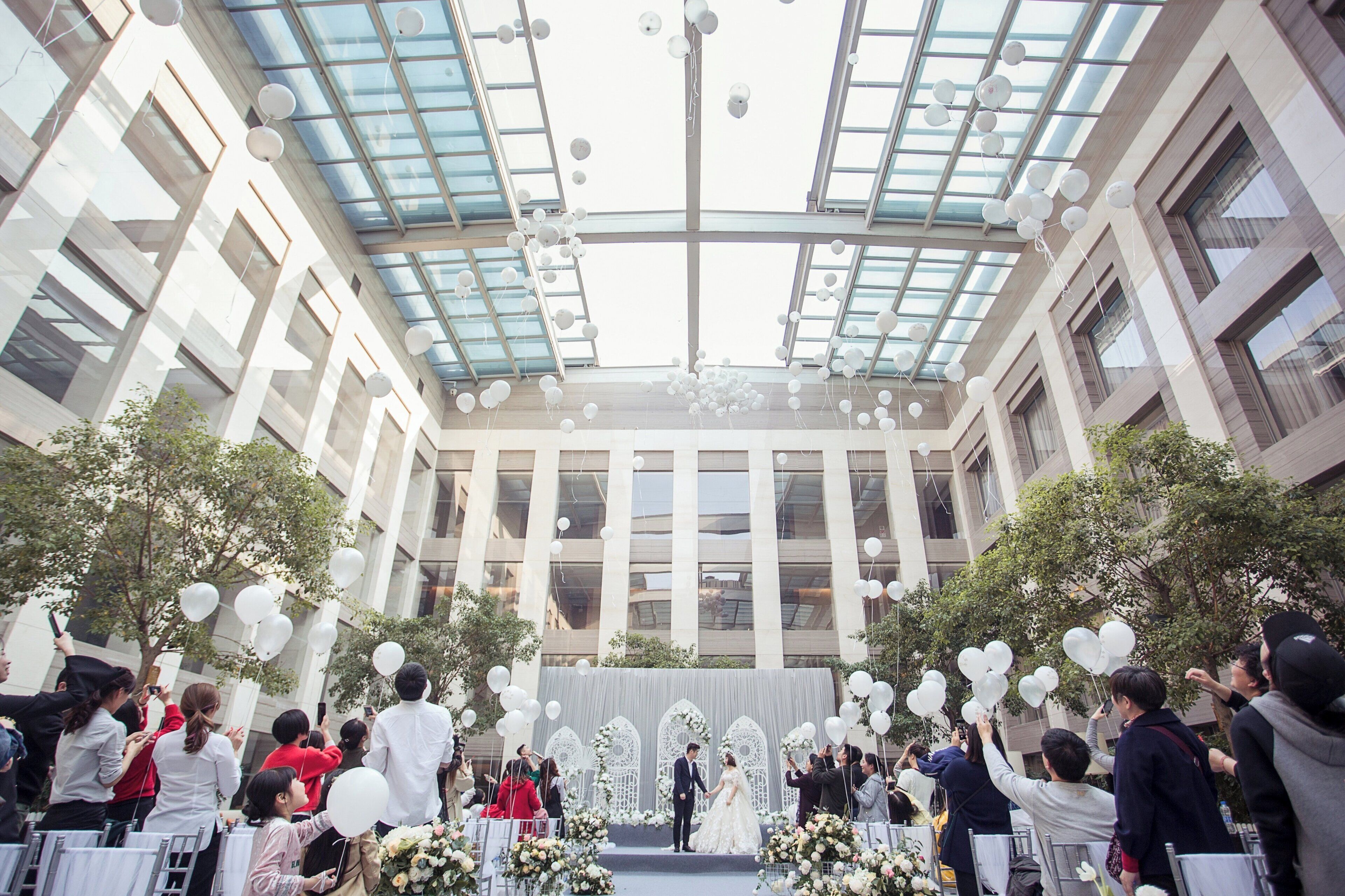 Una ceremonia de boda en un edificio moderno con techo de vidrio y un escenario para el evento.