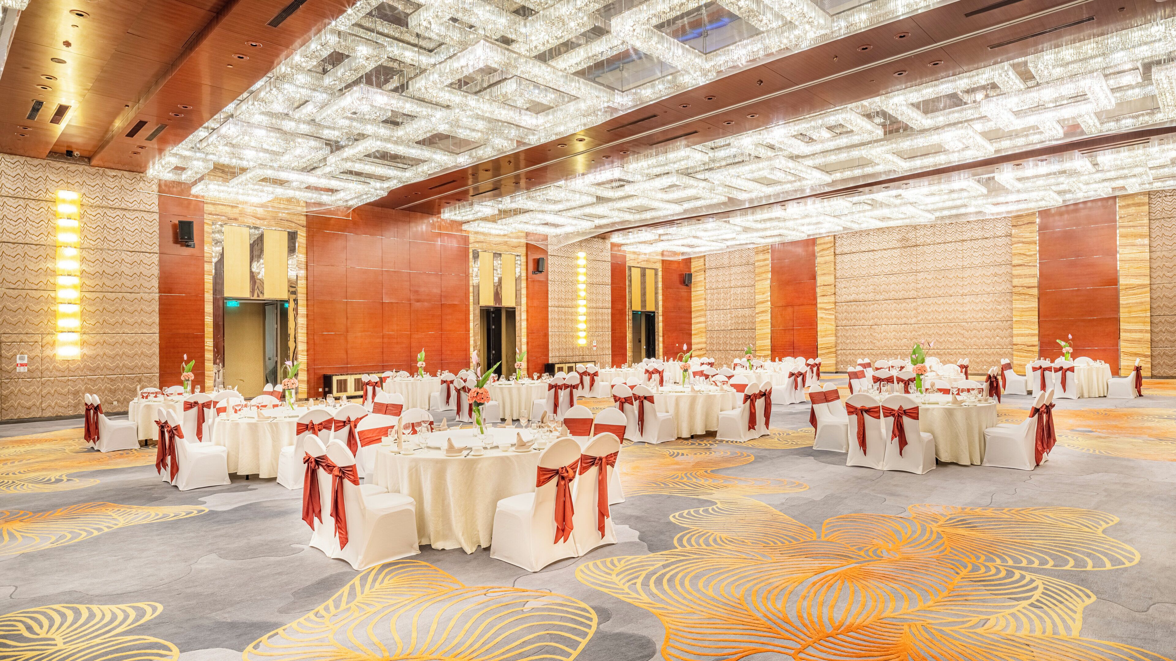 A large banquet hall with round tables, white tablecloths, and red sashes.