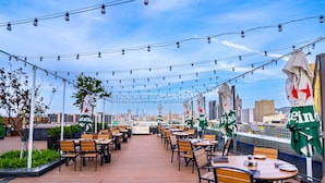 An outdoor dining area with tables and chairs, string lights, and flags.