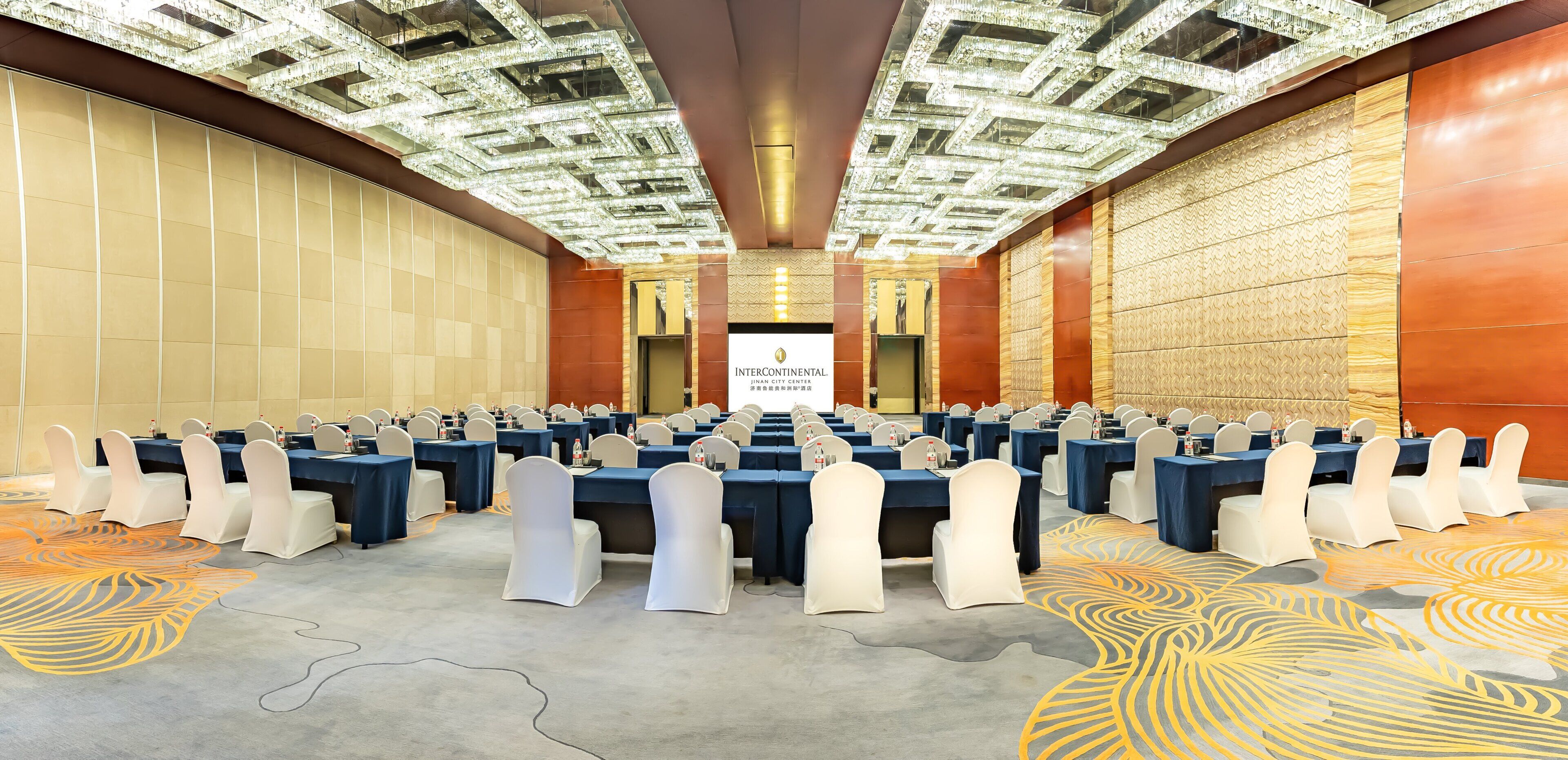 A conference room with multiple tables, chairs, and a large screen displaying 'INTERCONTINENTAL'.