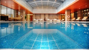 A large indoor swimming pool with a glass ceiling, lounge chairs, and a reception area.