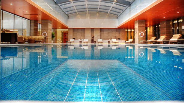 A large indoor swimming pool with a glass ceiling, lounge chairs, and a reception area. - InterContinental Jinan City Center by IHG (Jinan)