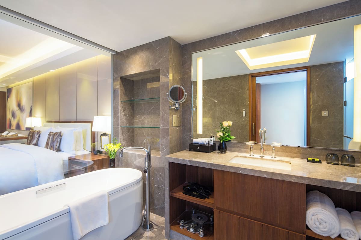 Ett modernt hotellbadrum med en stor spegel, ett badkar, en tvättställsmöbel med handfat och en duschhörna.