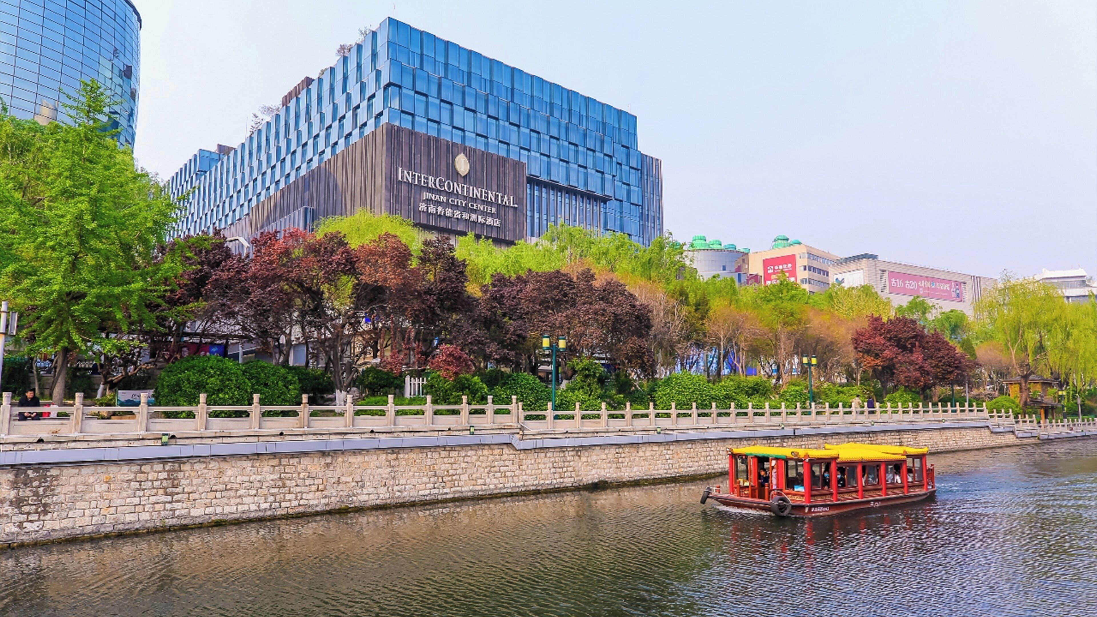 A river with a boat, a stone wall, and modern buildings including one with 'INTERCONTINENTAL' signage.