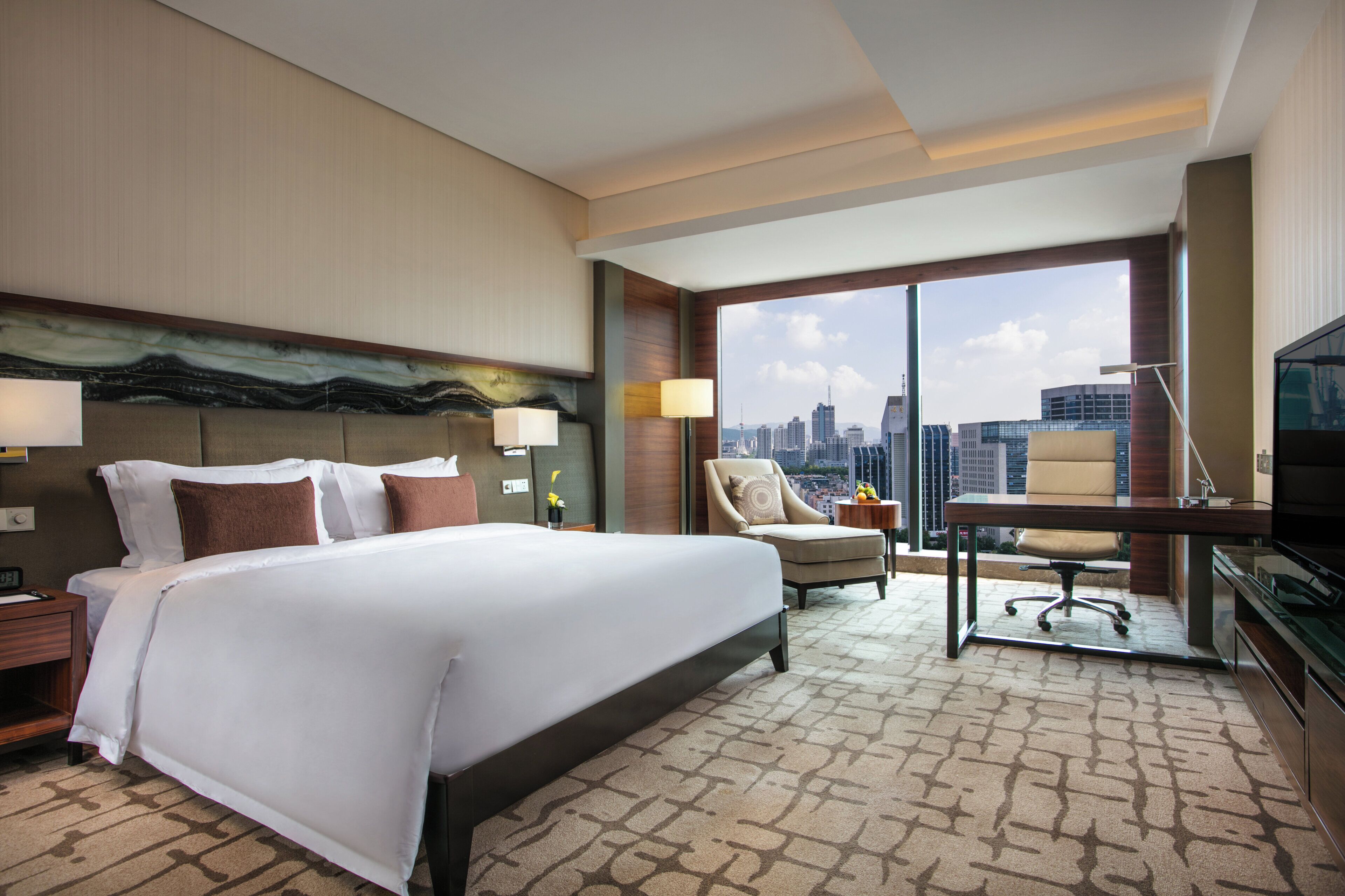 Une chambre d’hôtel avec un grand lit, un bureau avec une chaise, une télévision et une vue sur le paysage urbain.