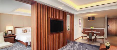 A hotel room with a bed, a TV, a dining area, and a wooden accent wall.