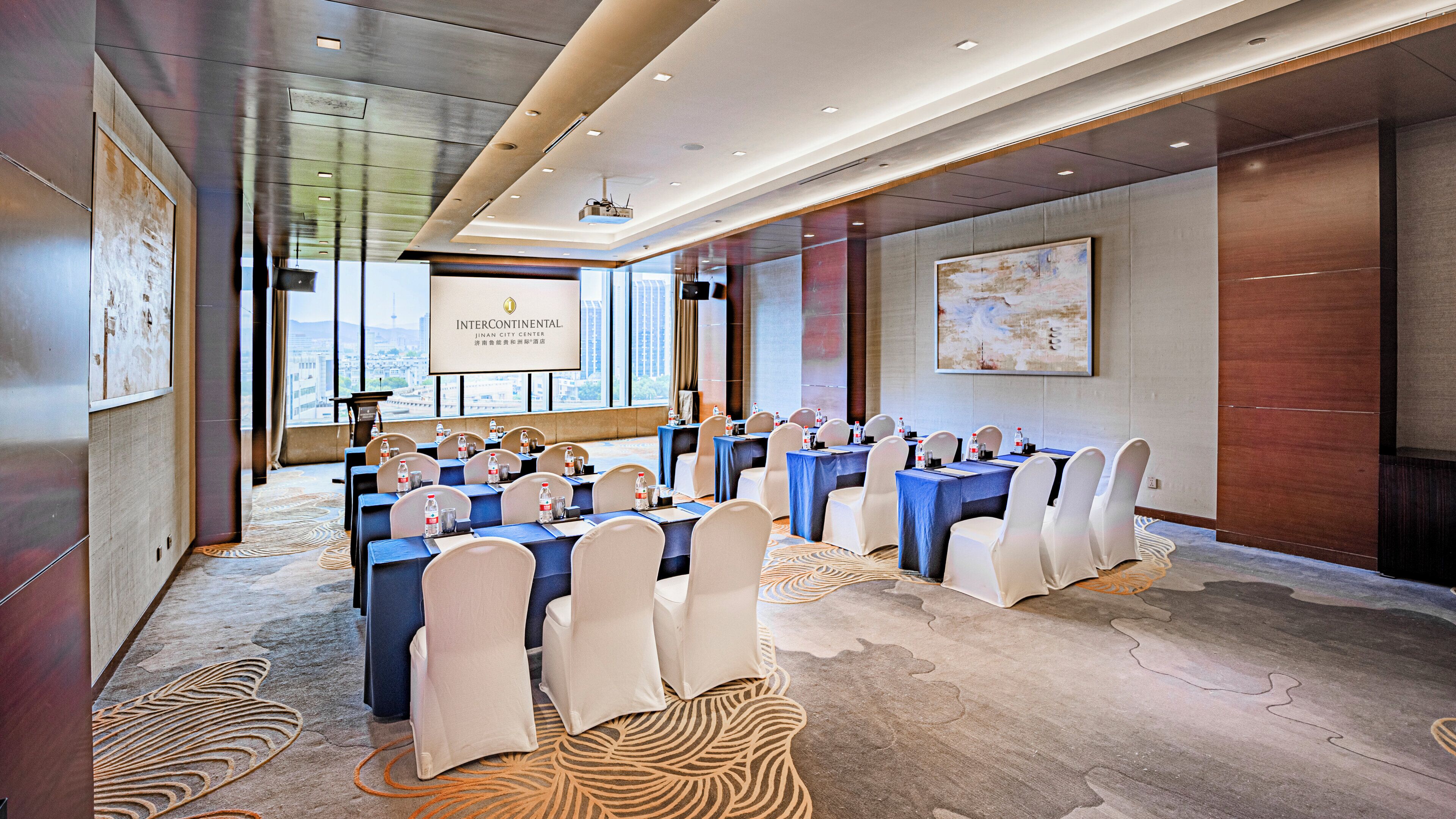 A conference room with tables set for meetings, a projector screen, and a city view.