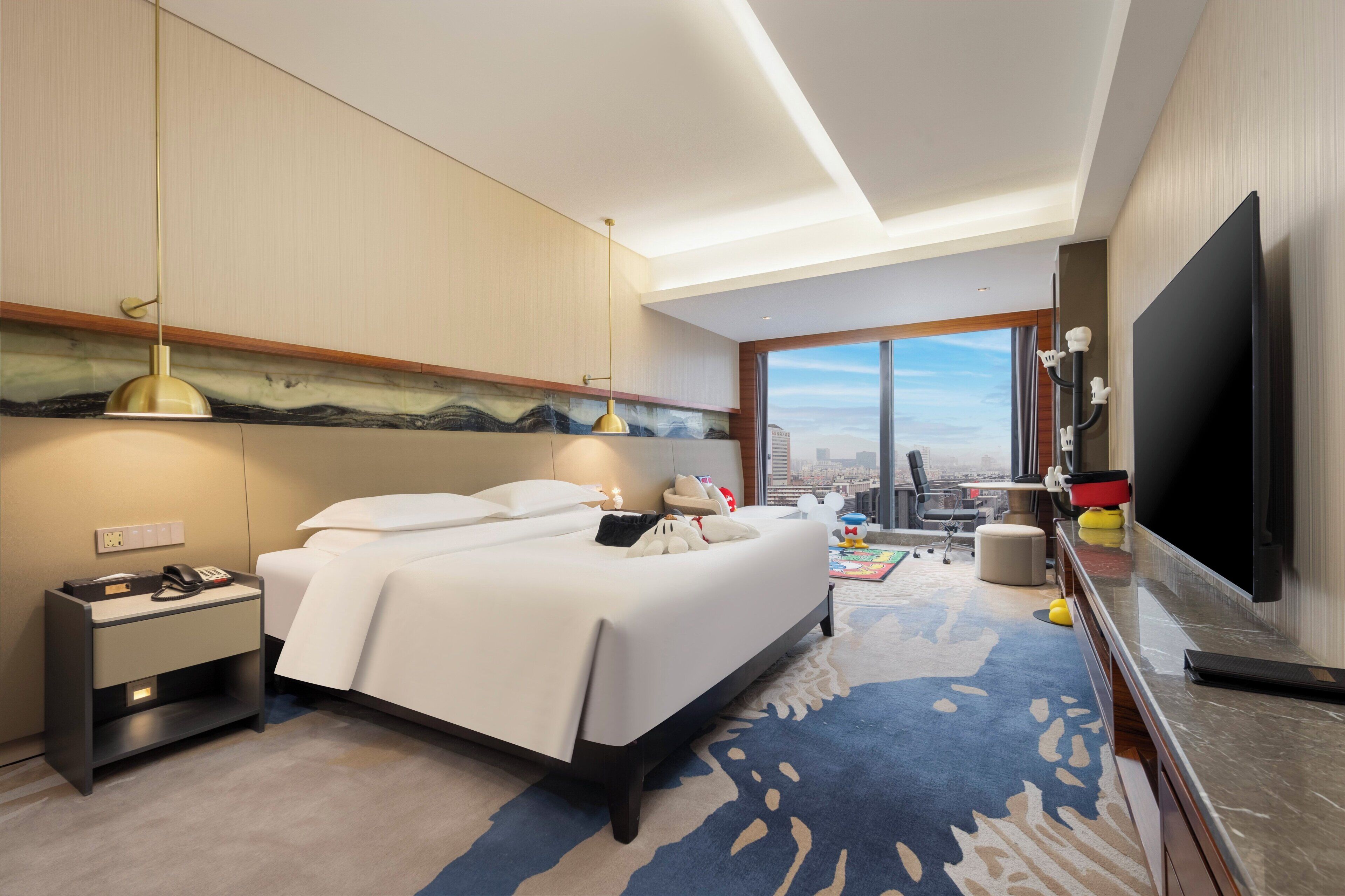 Una habitación de hotel moderna con una cama grande, un escritorio, un televisor de pantalla plana y vistas a la ciudad.