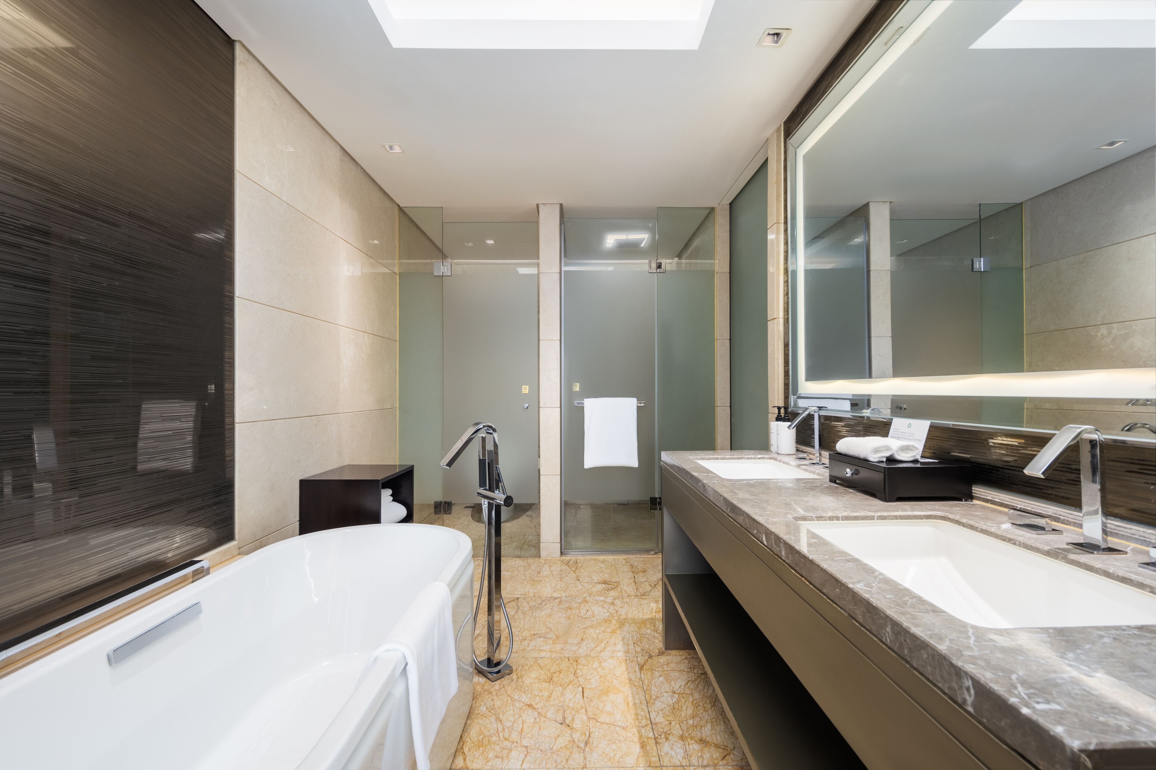 Een moderne badkamer met een groot bad, twee wastafels, een douchecabine met glazen wanden en een grote spiegel.
