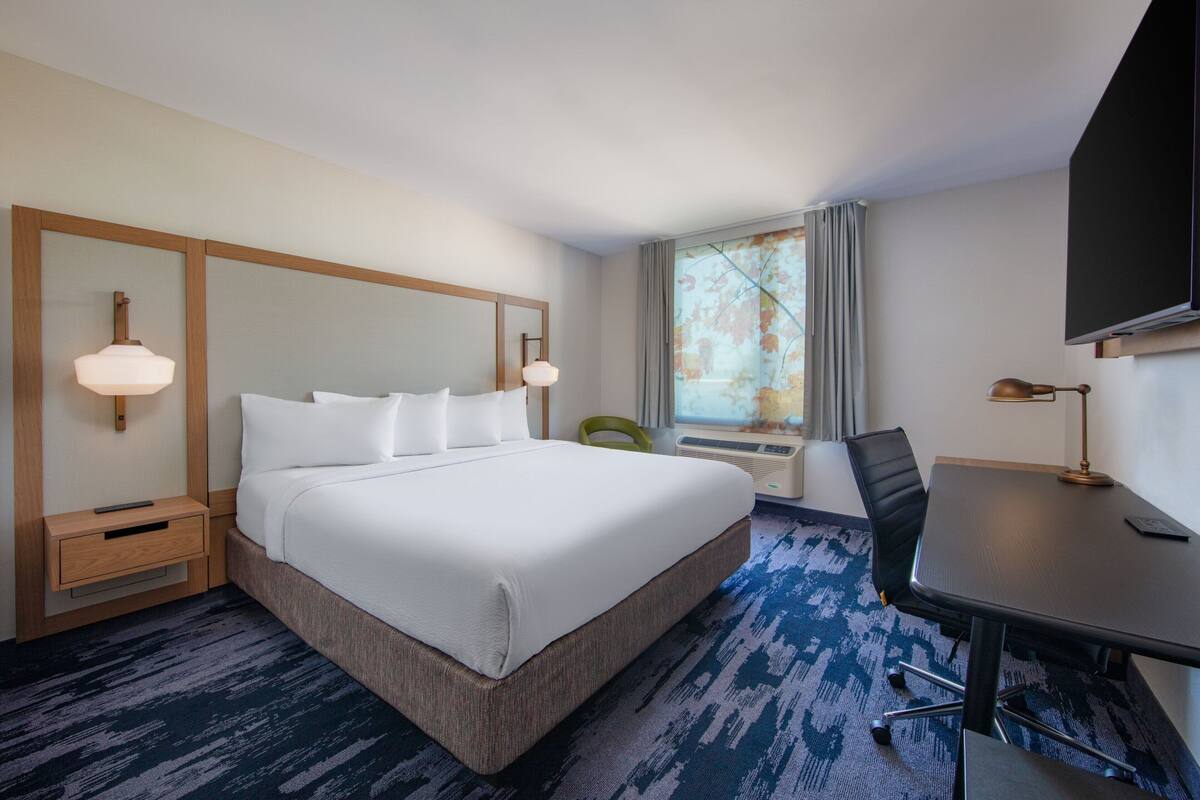 Une chambre d’hôtel avec un grand lit, des tables de chevet, un bureau, une chaise, une télévision et une fenêtre avec des rideaux.