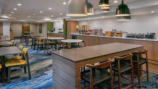 A modern hotel lobby with a central bar area, seating arrangements, and a tiled backsplash.