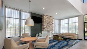 A modern living room with a stone fireplace, large windows, a round coffee table, and a beige sofa.