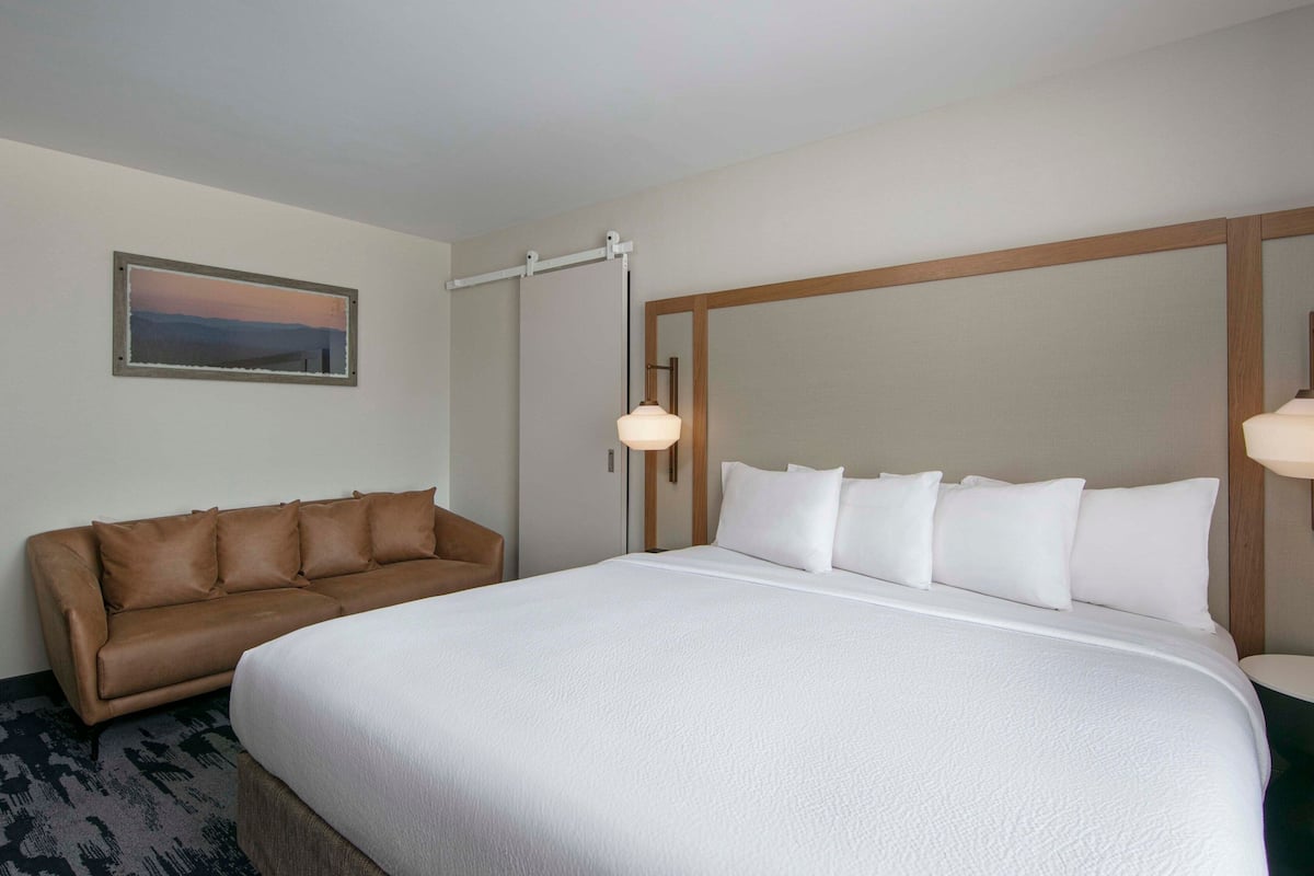 Une chambre d’hôtel avec un grand lit, un canapé en cuir marron, un tableau encadré au mur et une lampe de chevet.