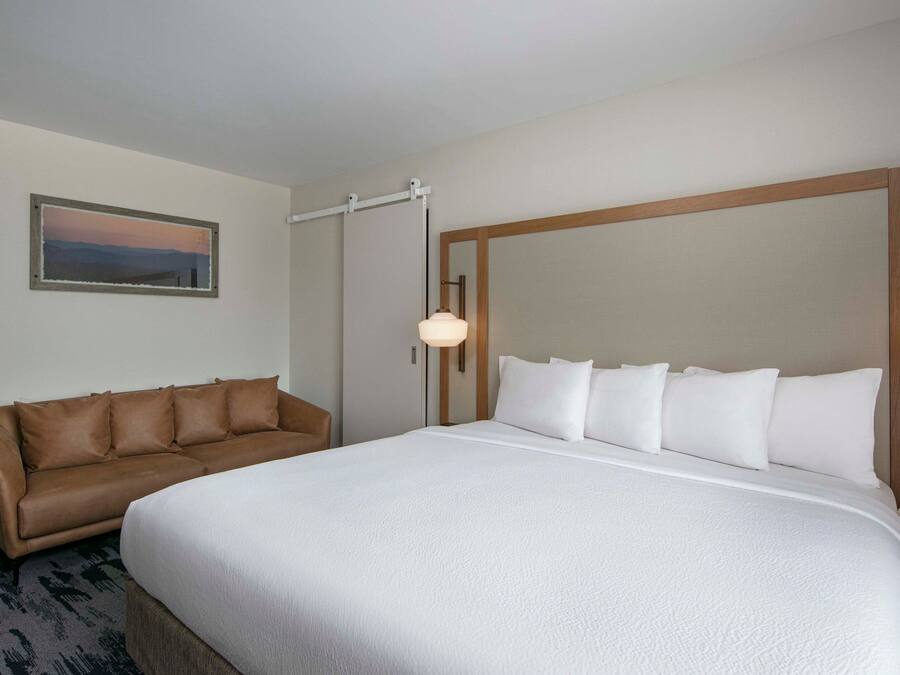 A hotel room with a large bed, a brown leather sofa, a framed picture on the wall, and a bedside lamp.