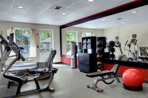 Ein Fitnessraum mit Trainingsgeräten, einem roten Übungsball und Blick ins Freie durch große Fenster.