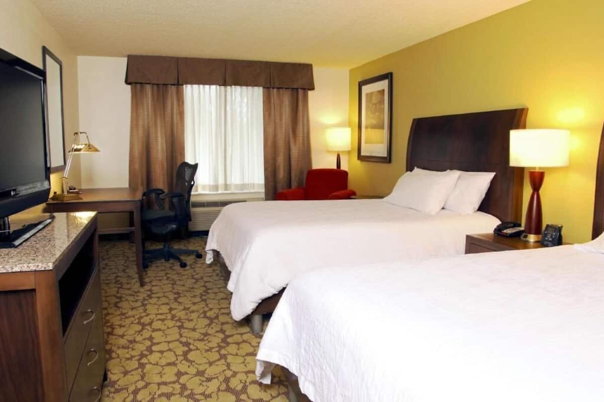 Une chambre d’hôtel avec deux lits, un bureau, une chaise, une télévision et une lampe.