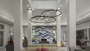 A spacious lobby with a high ceiling, modern lighting fixtures, and a central seating area with a patterned wall in the background.