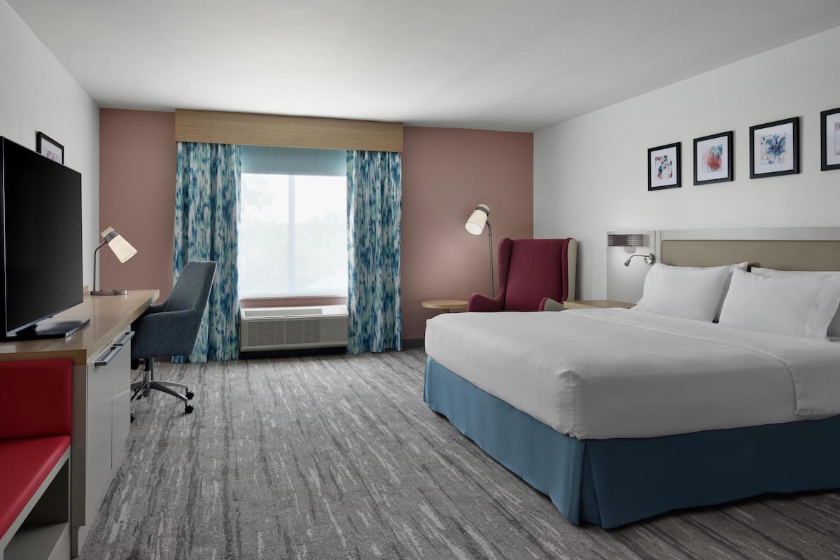 Une chambre d’hôtel équipée d’un lit, d’un bureau, d’une chaise, d’une télévision et d’œuvres d’art accrochées au mur.