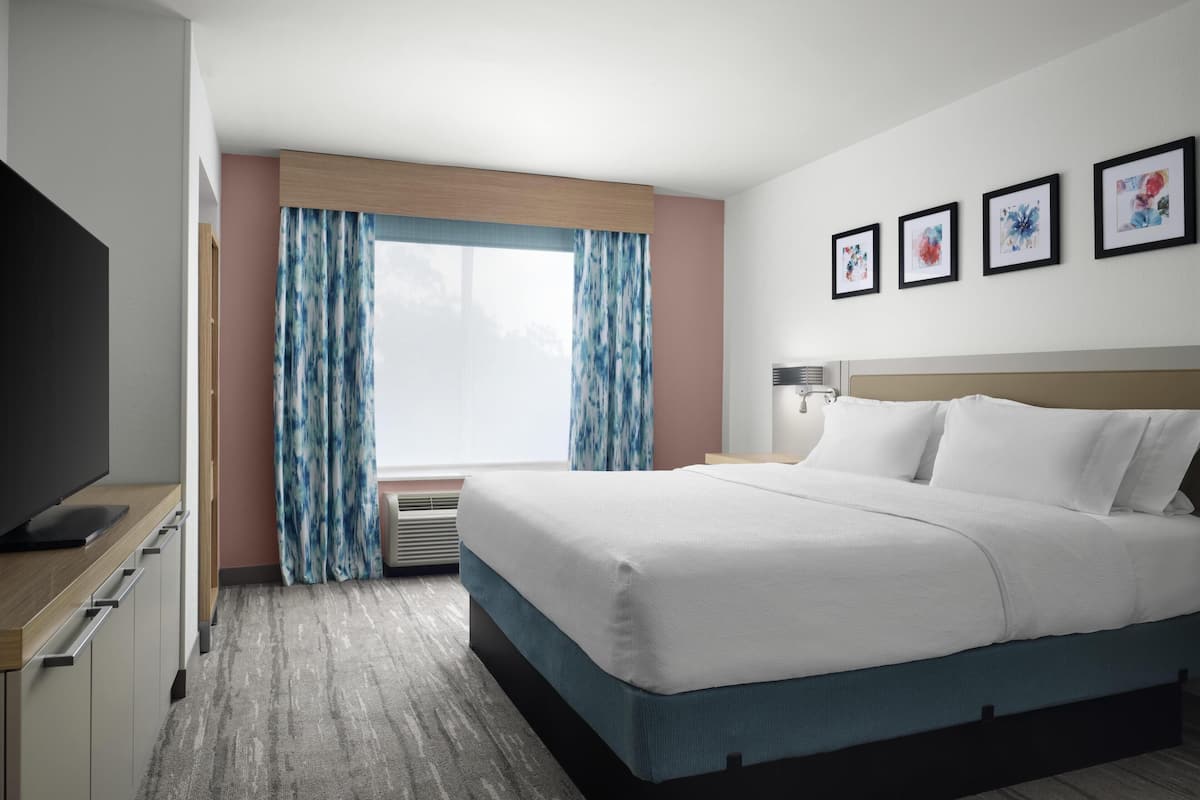 Une chambre d’hôtel avec un lit, une télévision, une fenêtre avec des rideaux et des œuvres d’art encadrées accrochées au mur.