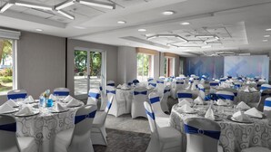 A banquet hall with round tables, white chairs with blue sashes, and a modern ceiling design.