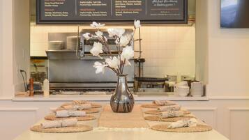Un restaurante con una pizarra de menú sobre la barra, un florero con flores en la mesa, y sillas de madera alrededor de la mesa.