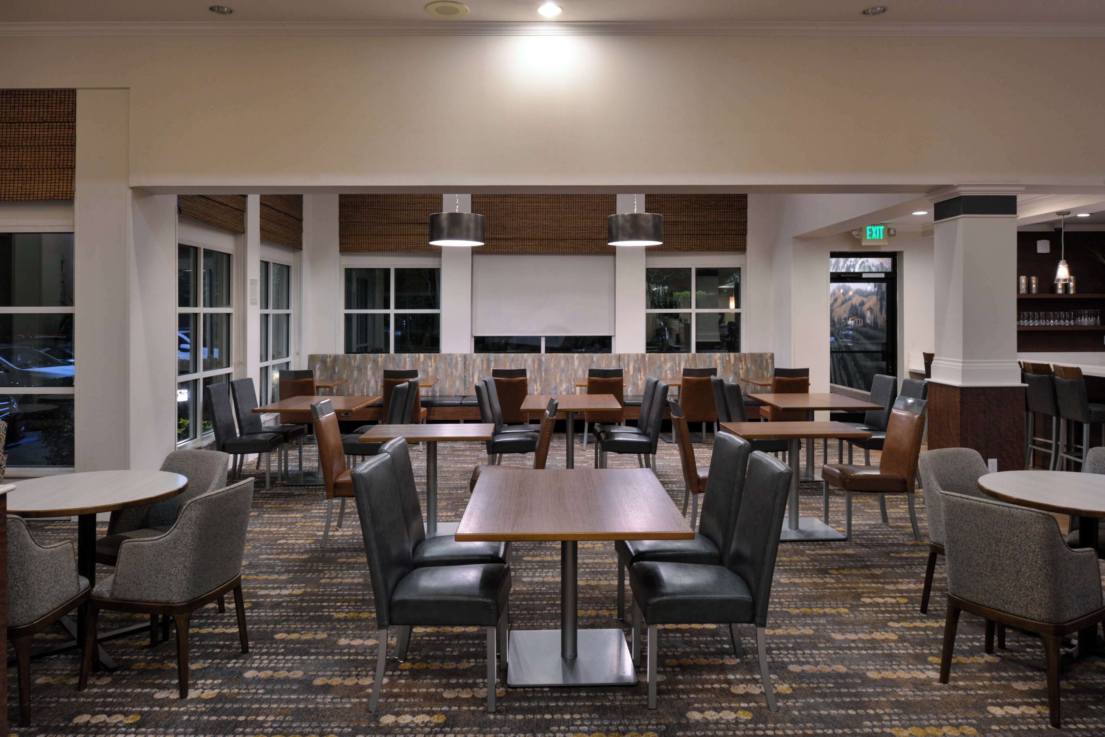 A hotel lobby with multiple seating areas, including tables and chairs, and a large windowed wall.