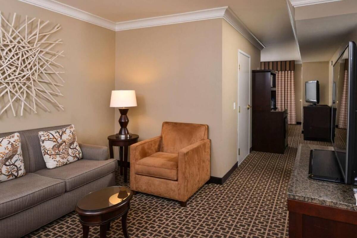 A hotel room with a sofa, armchair, lamp, and a small table. There is a television and a mirror on the wall.