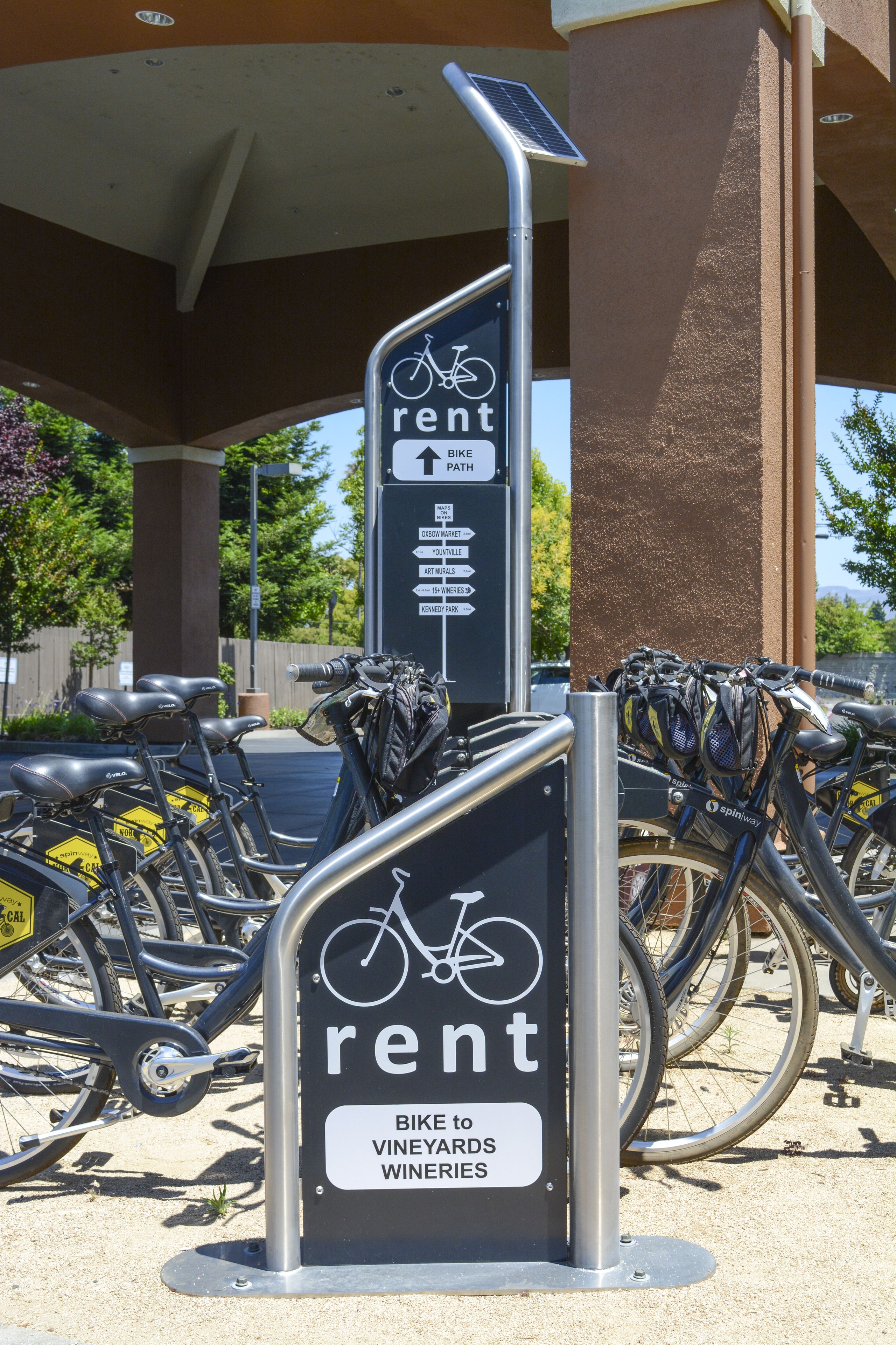 A bike rental station with a sign indicating directions to vineyards and wineries.