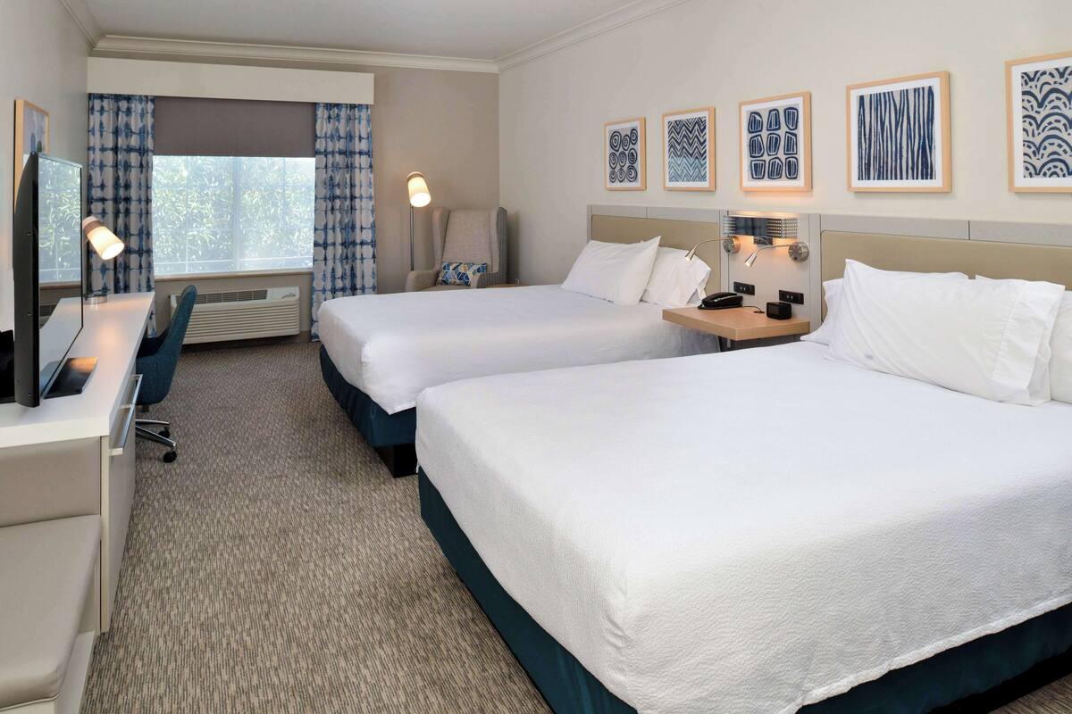 A hotel room with two beds, a desk with a computer, a chair, and a window with curtains.