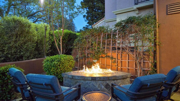 A patio with two rocking chairs and a small table, surrounded by lush greenery and a fire feature. - Hilton Garden Inn Napa (Napa)