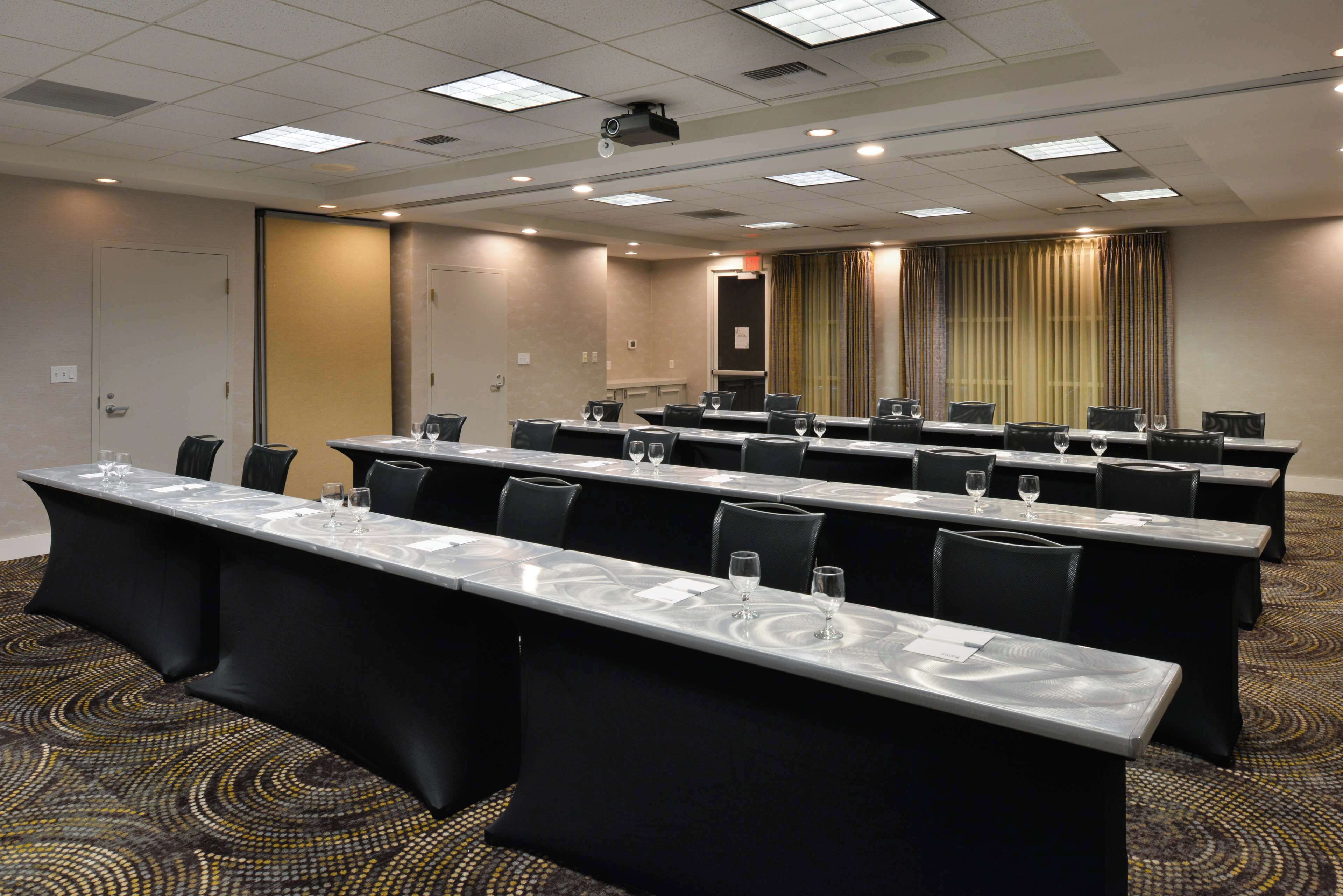 Un salón de conferencias con mesas largas, sillas y una pantalla para proyector.