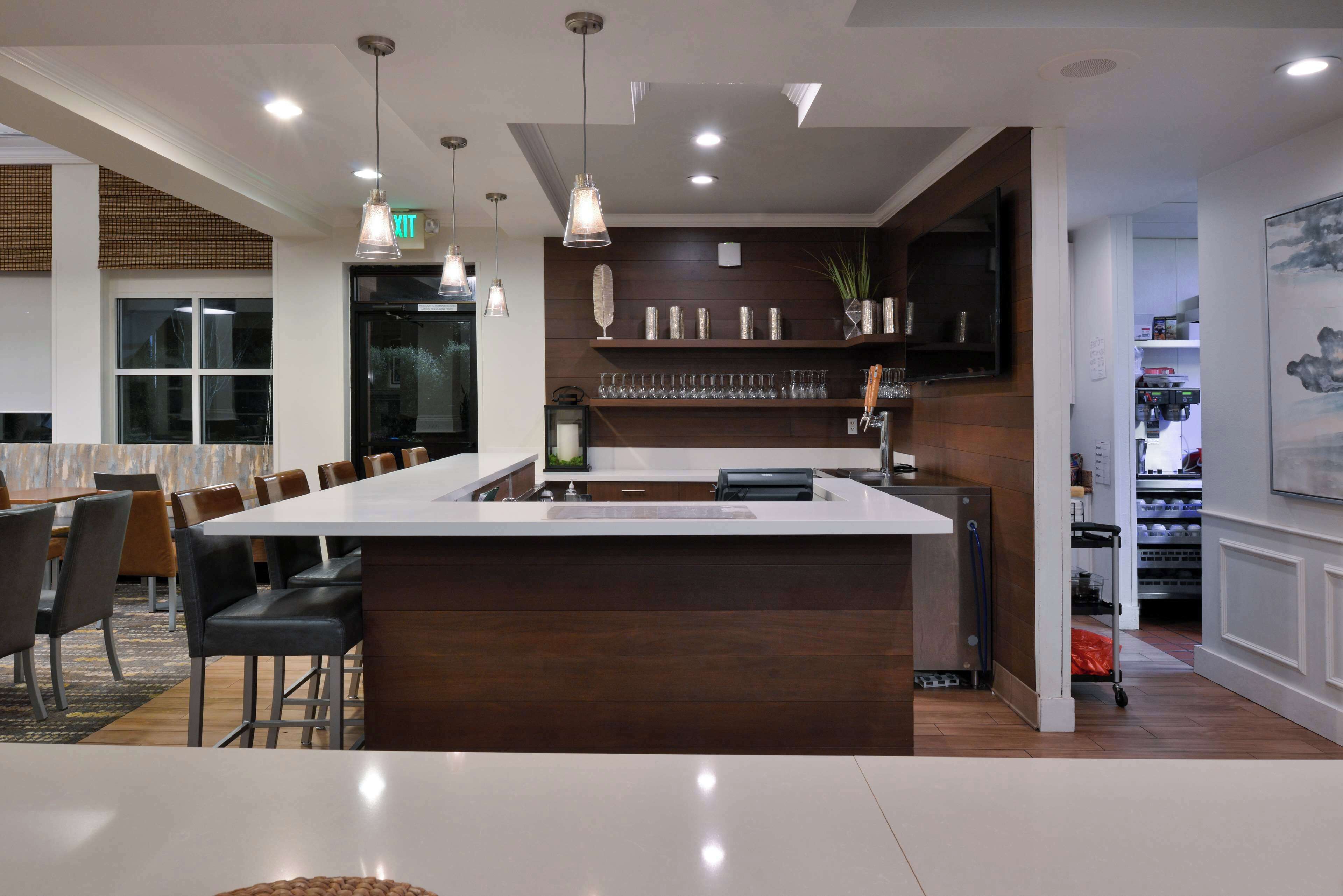 A modern kitchen with a central island, pendant lighting, and a dining area with chairs and tables.
