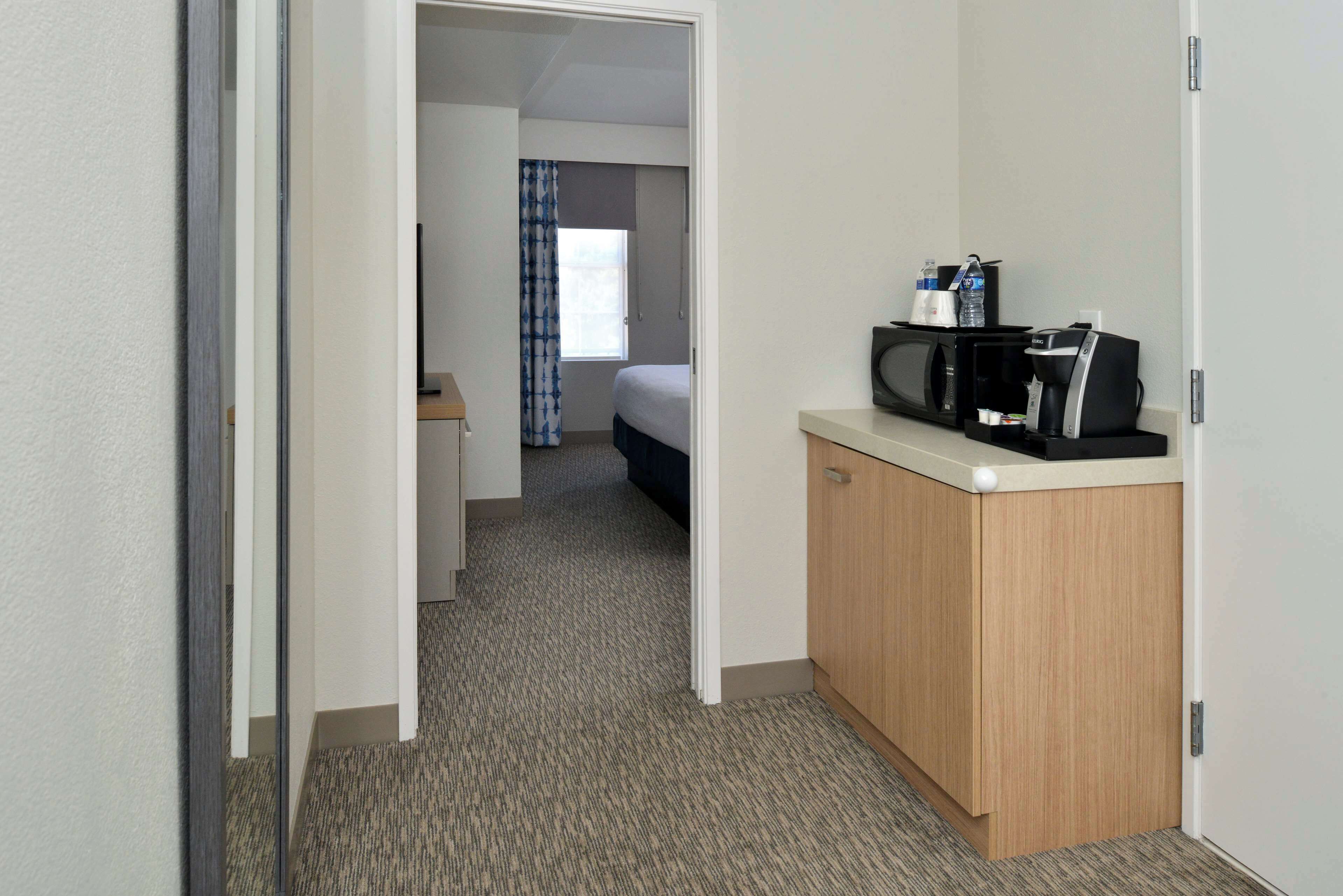 Habitación de hotel con una cama, un pequeño escritorio con cafetera y vista al pasillo.