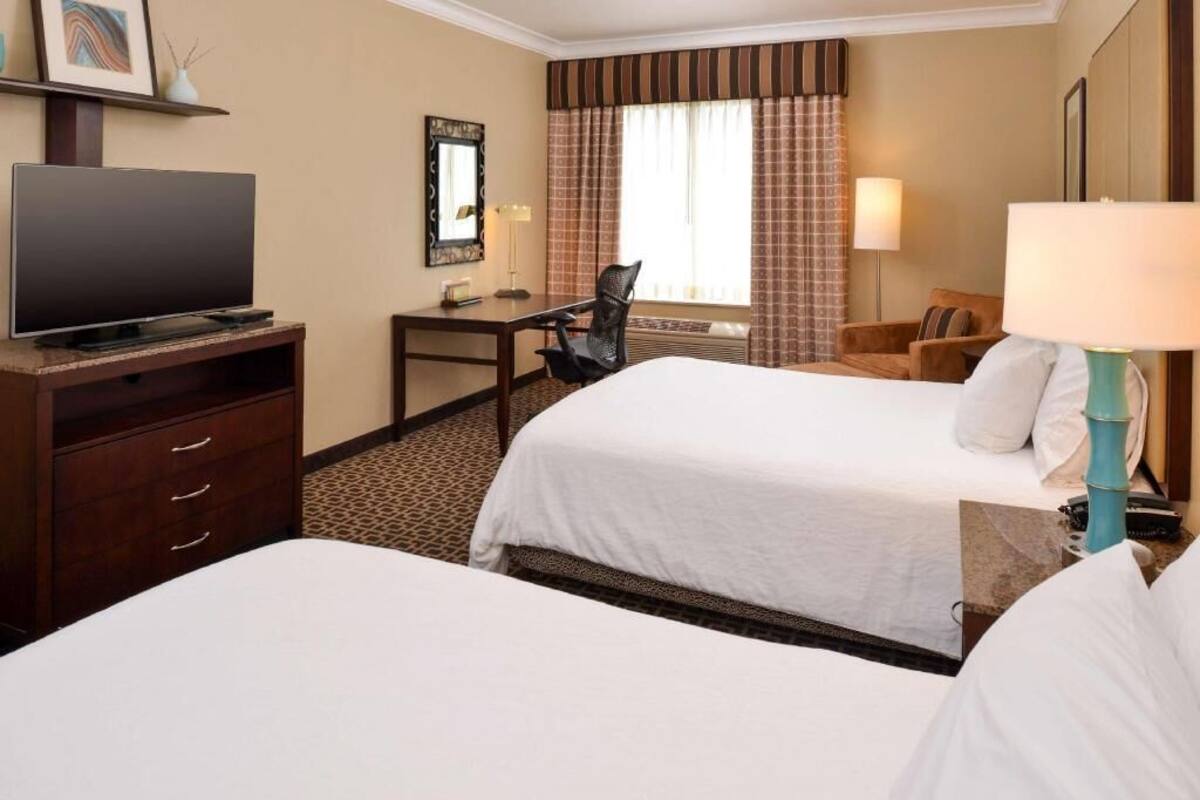 A hotel room with two beds, a desk, a television, and a lamp.