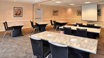 A conference room with multiple tables and chairs, a projector screen, and framed pictures on the walls.
