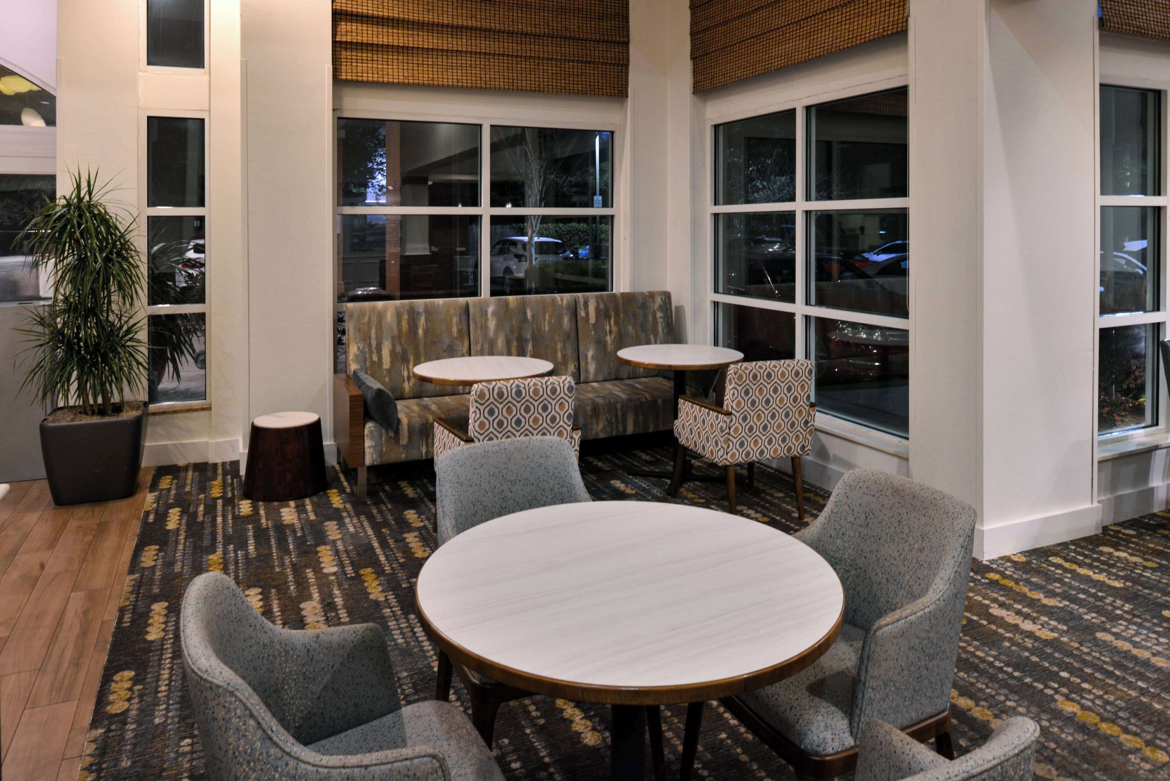A hotel lobby with a seating area, two round tables, and a large window with a view of parked cars.