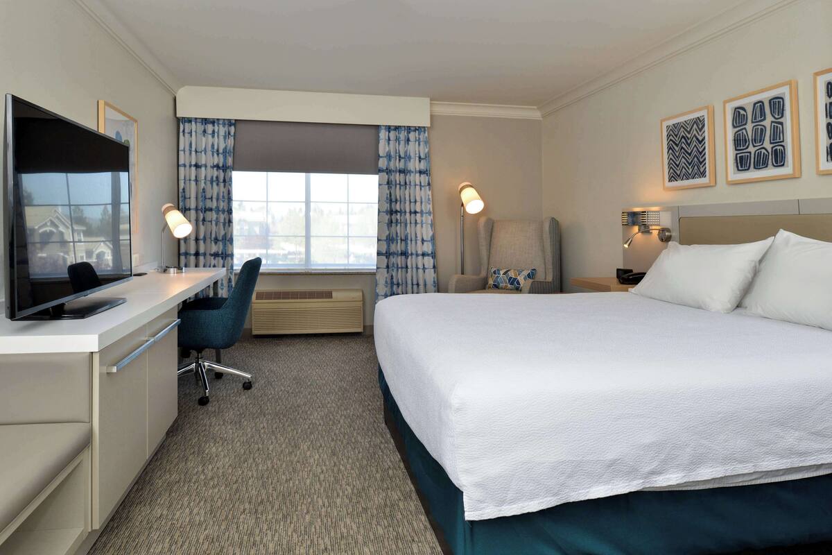 A hotel room with a bed, desk, chair, TV, and a window with curtains.