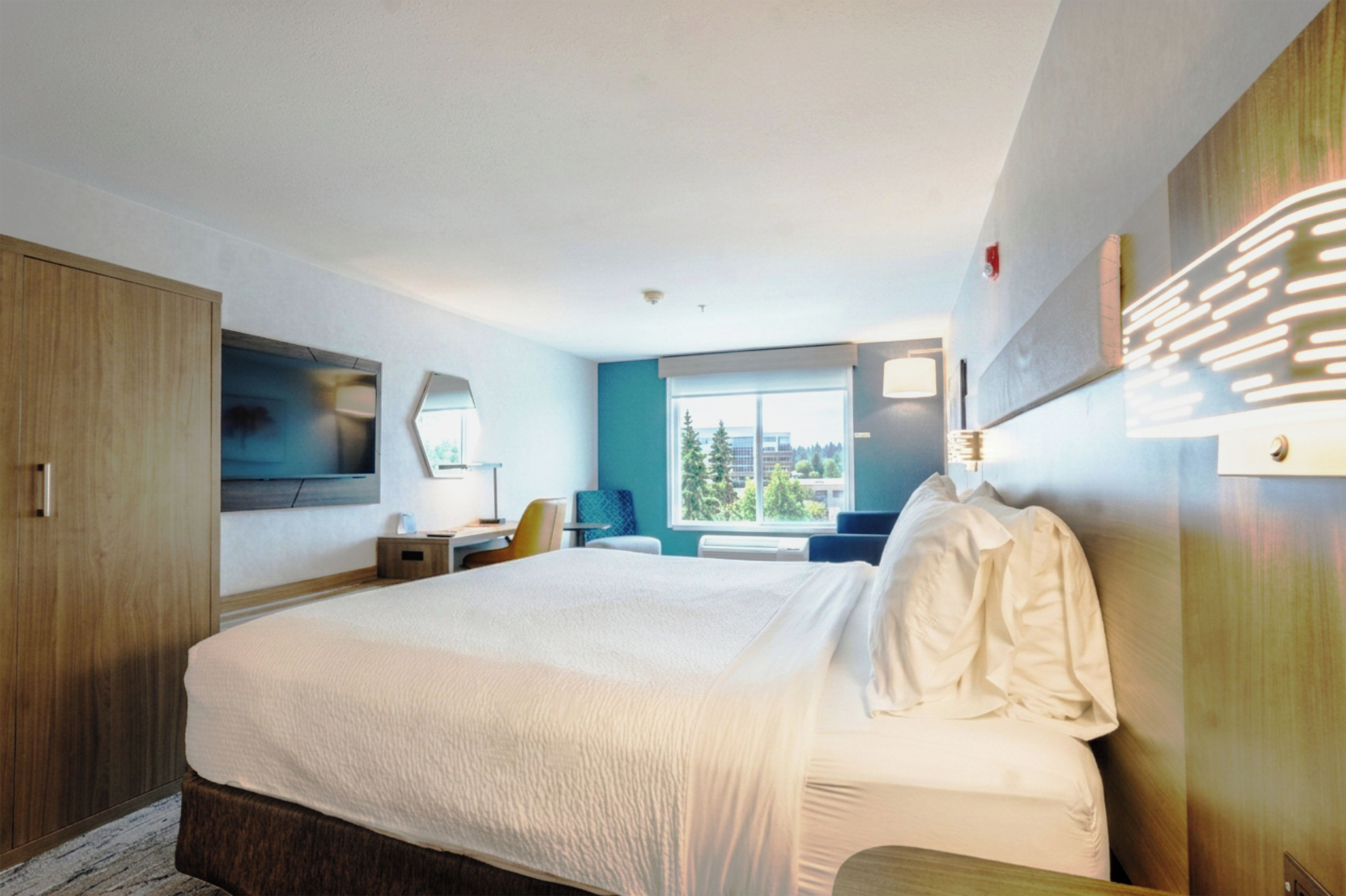 Une chambre d’hôtel avec un grand lit, un bureau, une chaise, une télévision et une fenêtre donnant sur des immeubles.