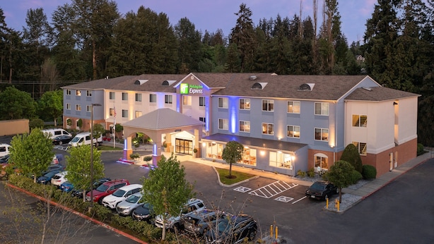 A Holiday Inn Express hotel with a parking lot, multiple floors, and a surrounding forest. - Holiday Inn Express Bothell by IHG (Bothell)