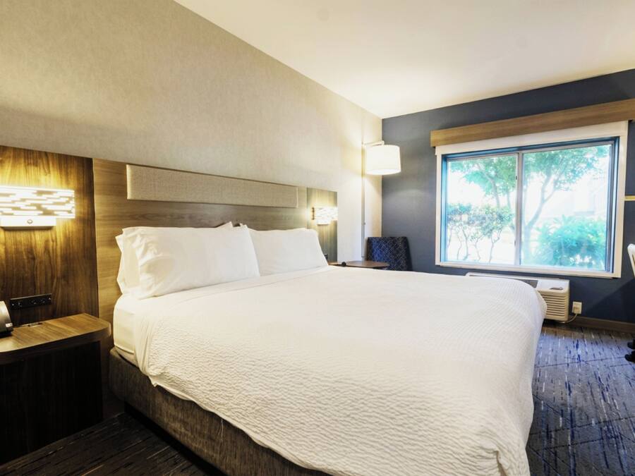 Habitación de hotel con una cama grande, mesitas de noche, un escritorio, una silla, un ventanal con vistas y una lámpara de pared.
