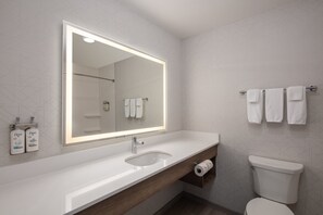 A modern bathroom with a large mirror, white sink, wooden vanity, and a toilet.
