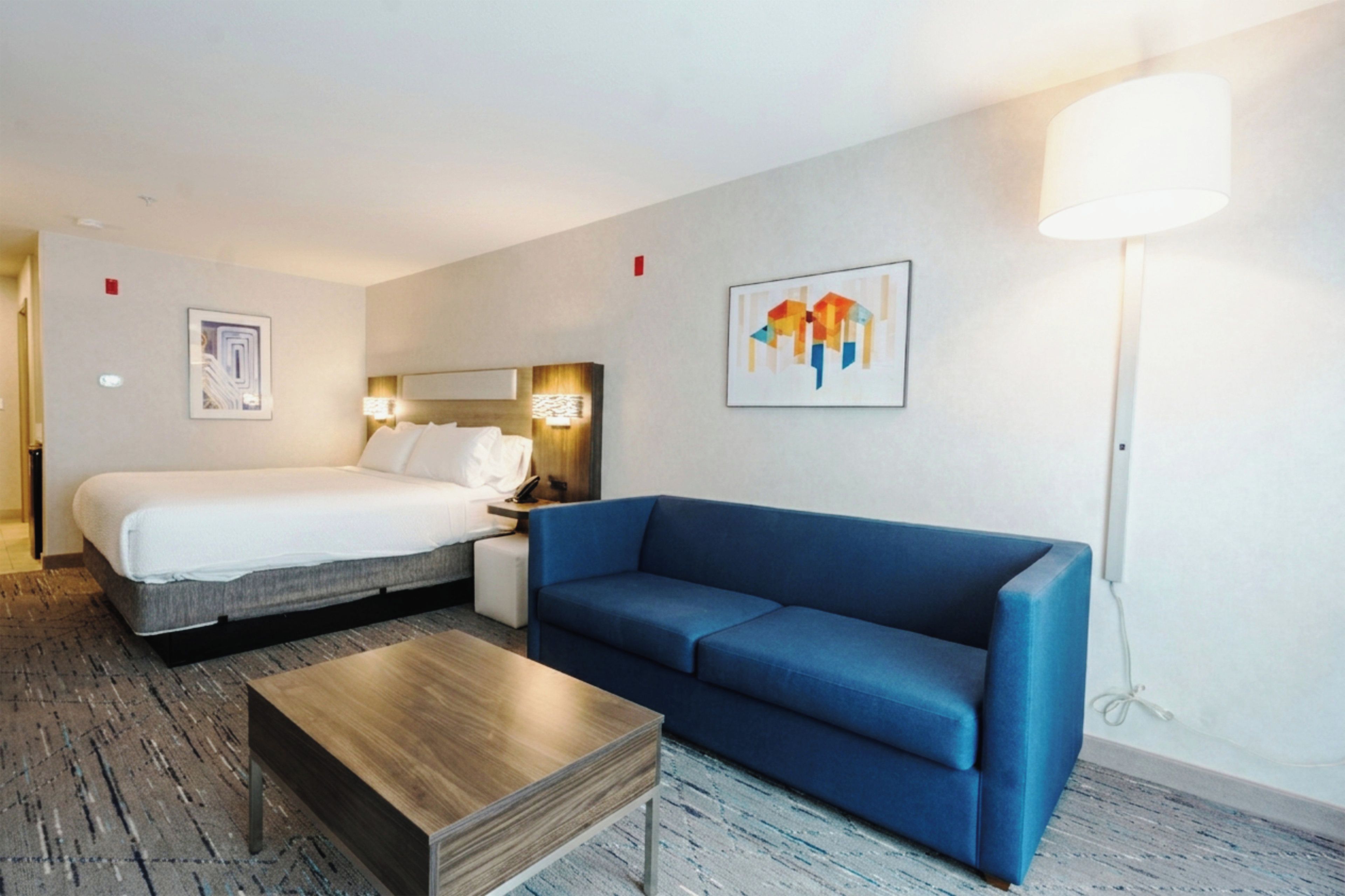 A hotel room with a bed, a blue sofa, a wooden coffee table, and a painting on the wall.