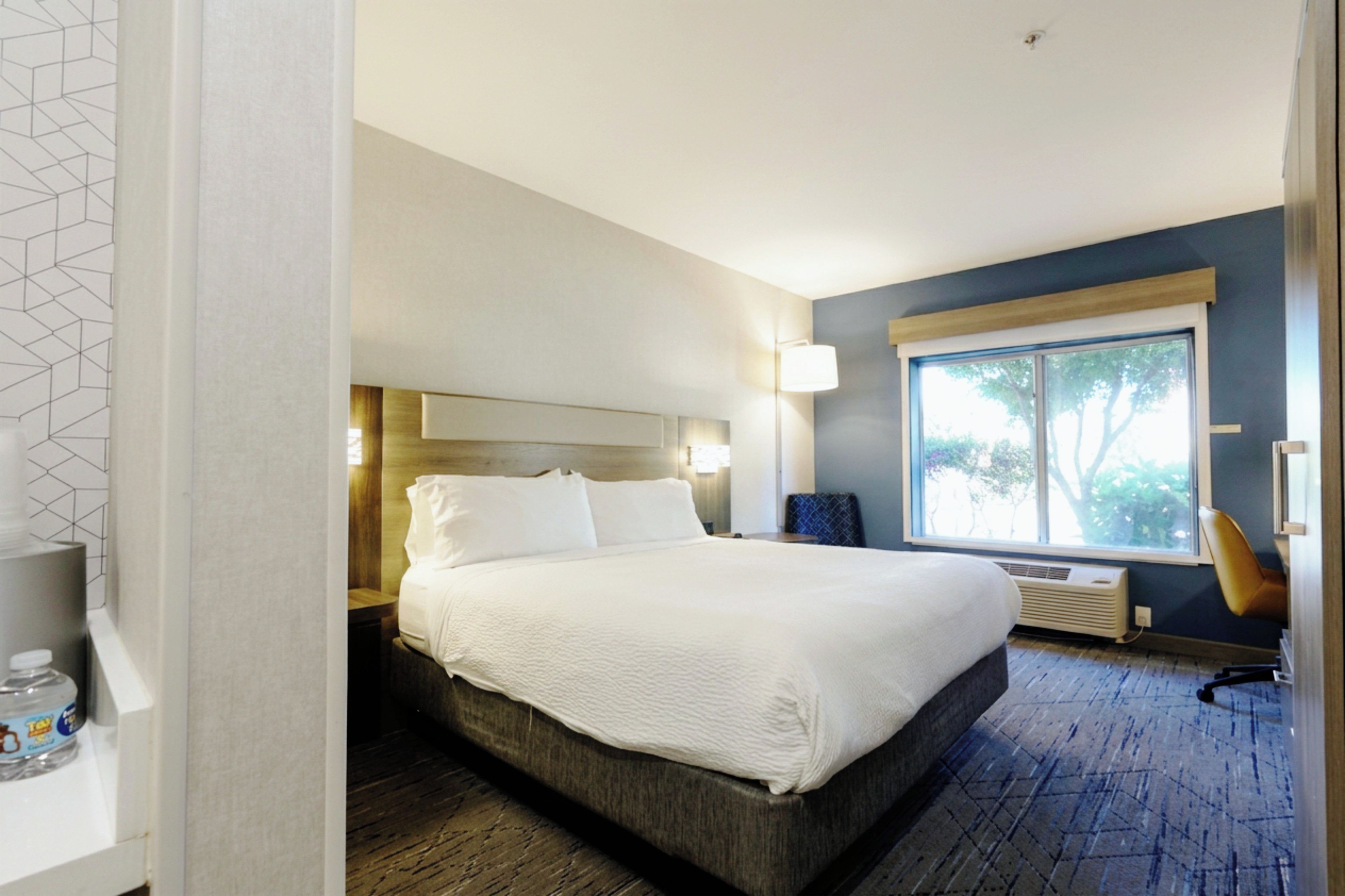 A hotel room with a large bed, a window with a view, a bedside table, and a chair.