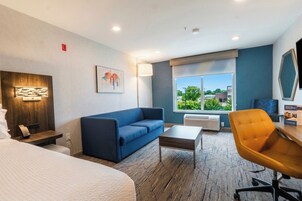 Ein Hotelzimmer mit Bett, blauem Sofa, Holztisch, Stuhl, Lampe und Fenster mit Blick.