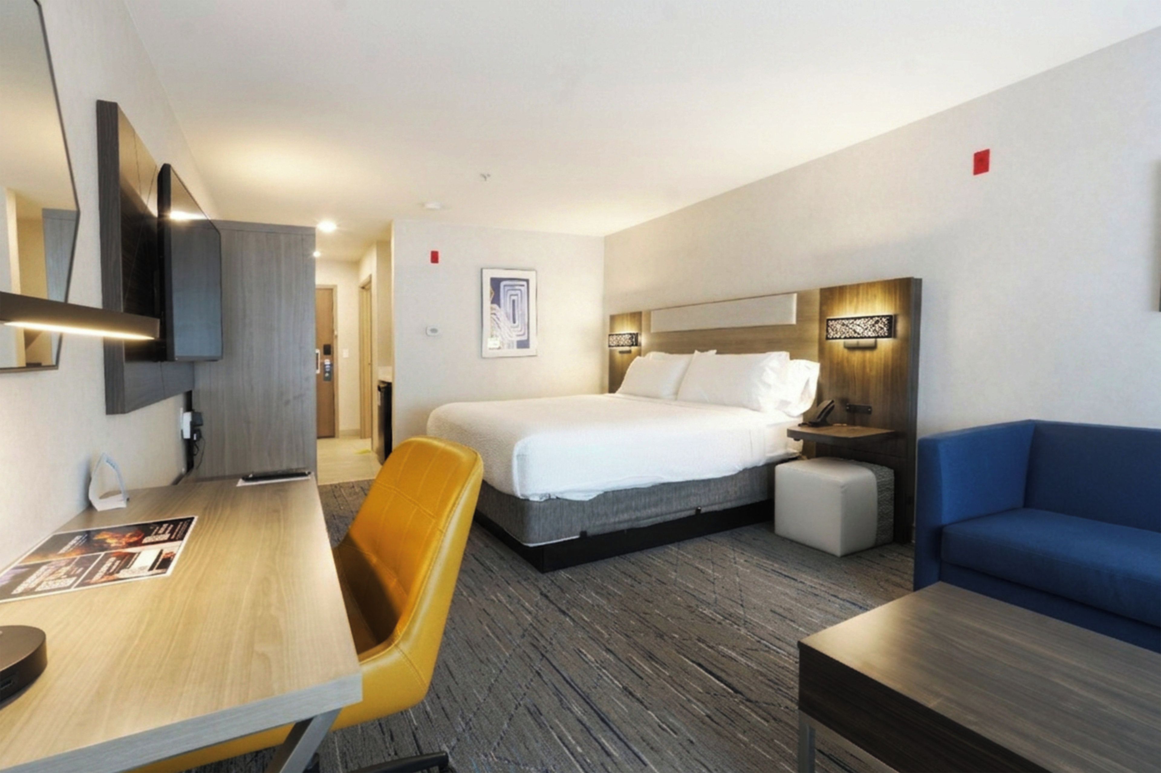 A hotel room with a bed, a desk, a chair, a sofa, and a bedside table.