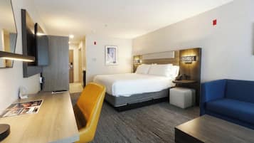 A hotel room with a bed, a desk, a chair, a sofa, and a bedside table.