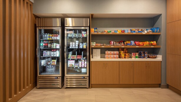 Eine Selbstbedienungsstation für Getränke mit zwei gekühlten Getränkespendern und Regalen voller Snacks und Getränken.
