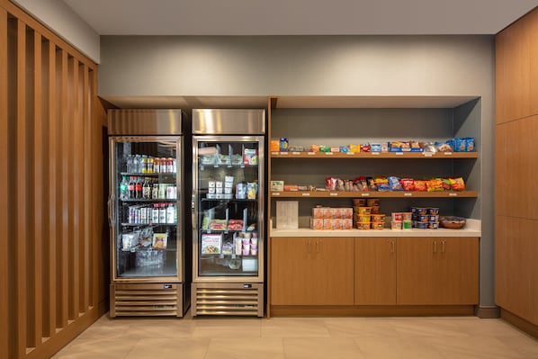 A self-service beverage station with two refrigerated drink dispensers and shelves stocked with snacks and beverages. - Holiday Inn Express Bothell by IHG (Bothell)