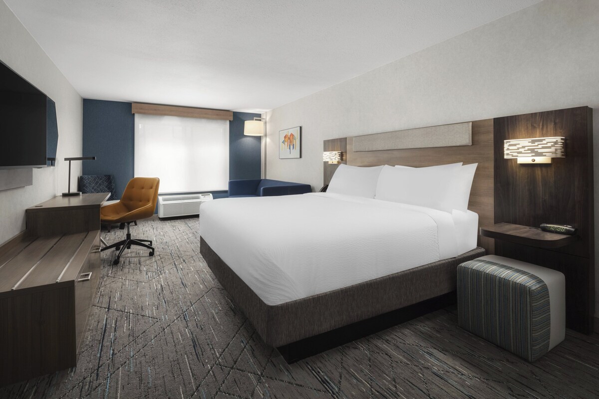 A modern hotel room with a large bed, a desk, a chair, and a TV.
