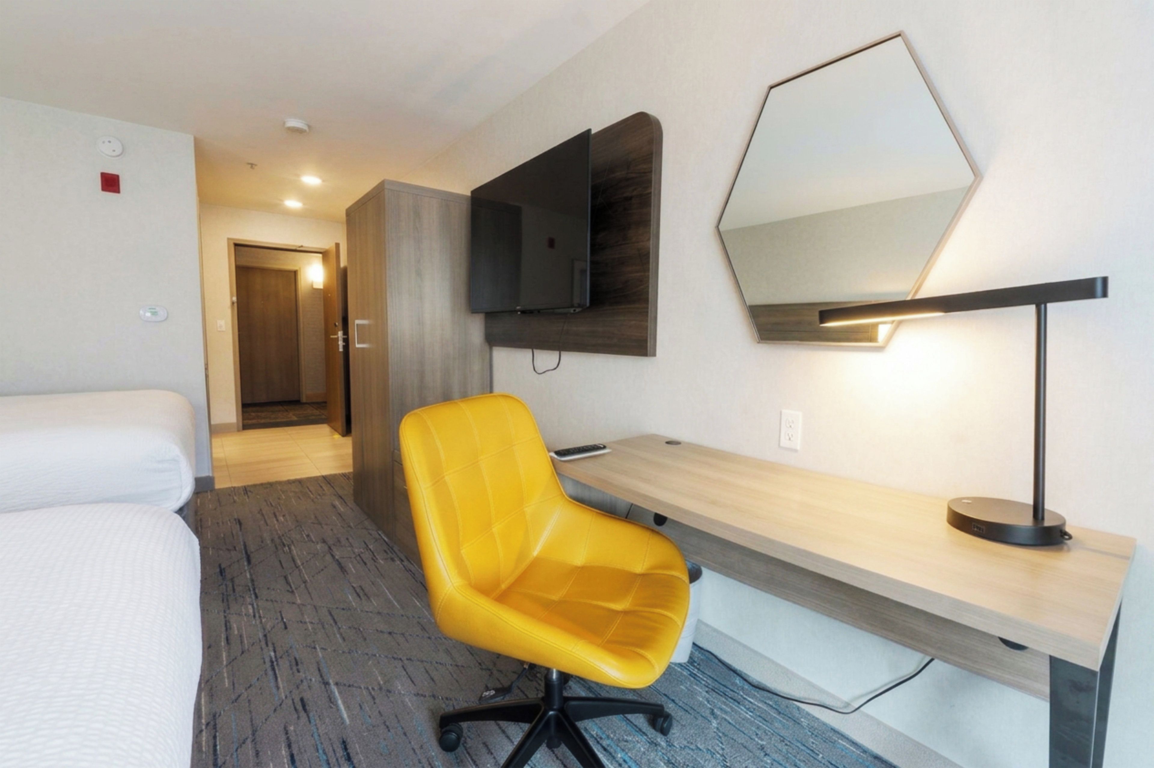 A hotel room with a bed, a desk, a chair, a television, and a mirror.